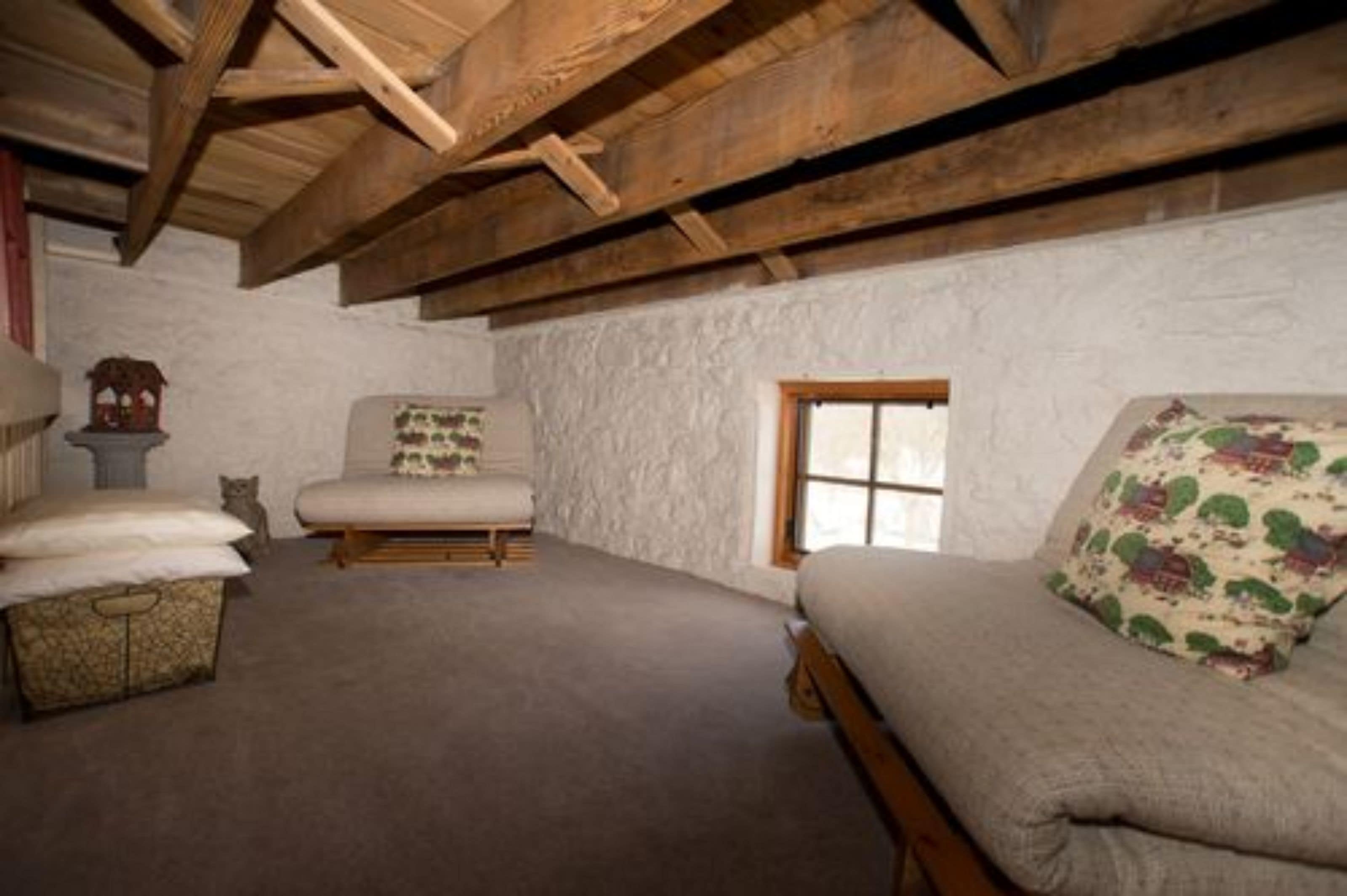 A rustic room with a sloped ceiling, a wooden bench, a cushioned chair, and a small window.
