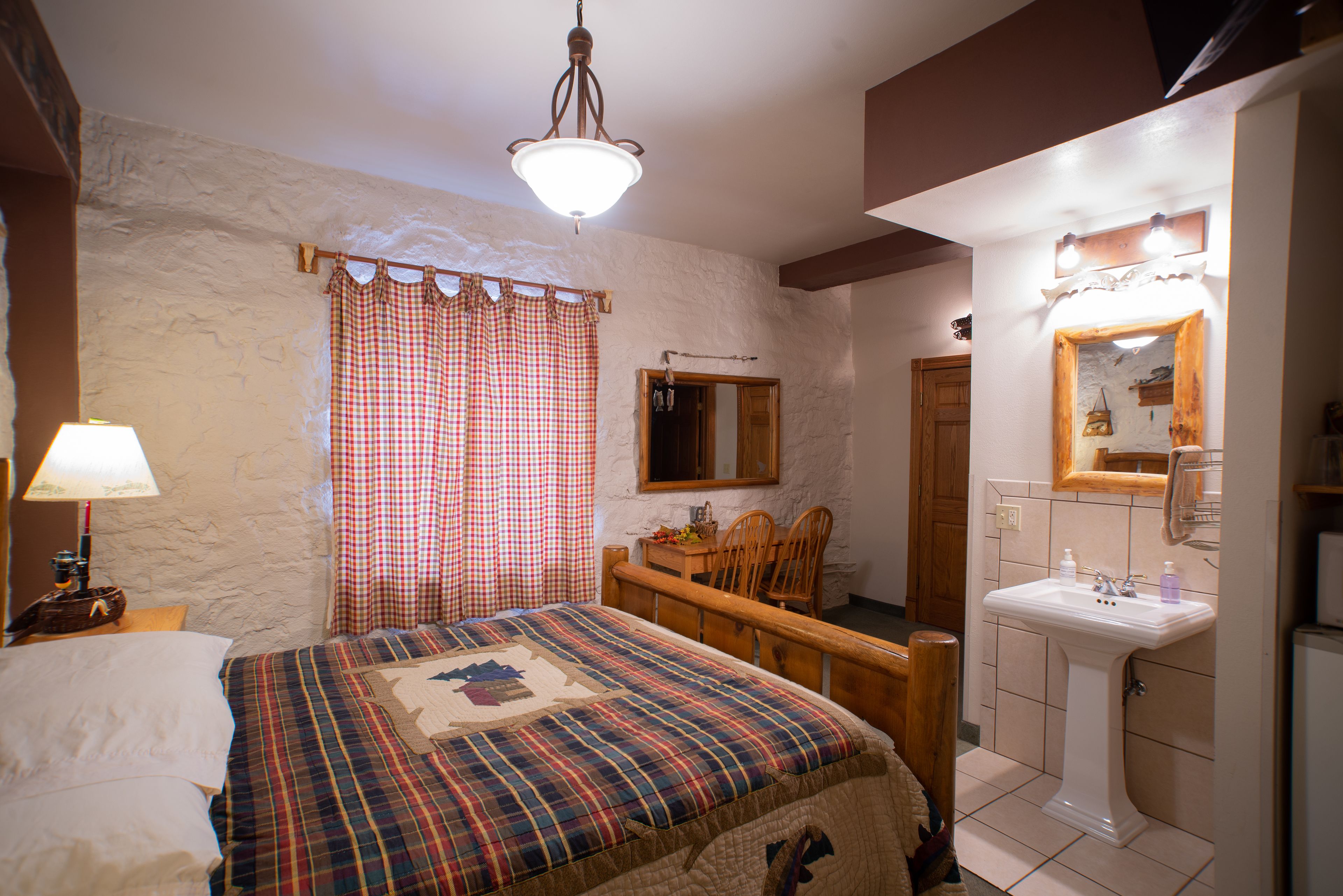 Een slaapkamer met een bed, nachtkastje, kapstok en badkamer met een wastafel en spiegel.
