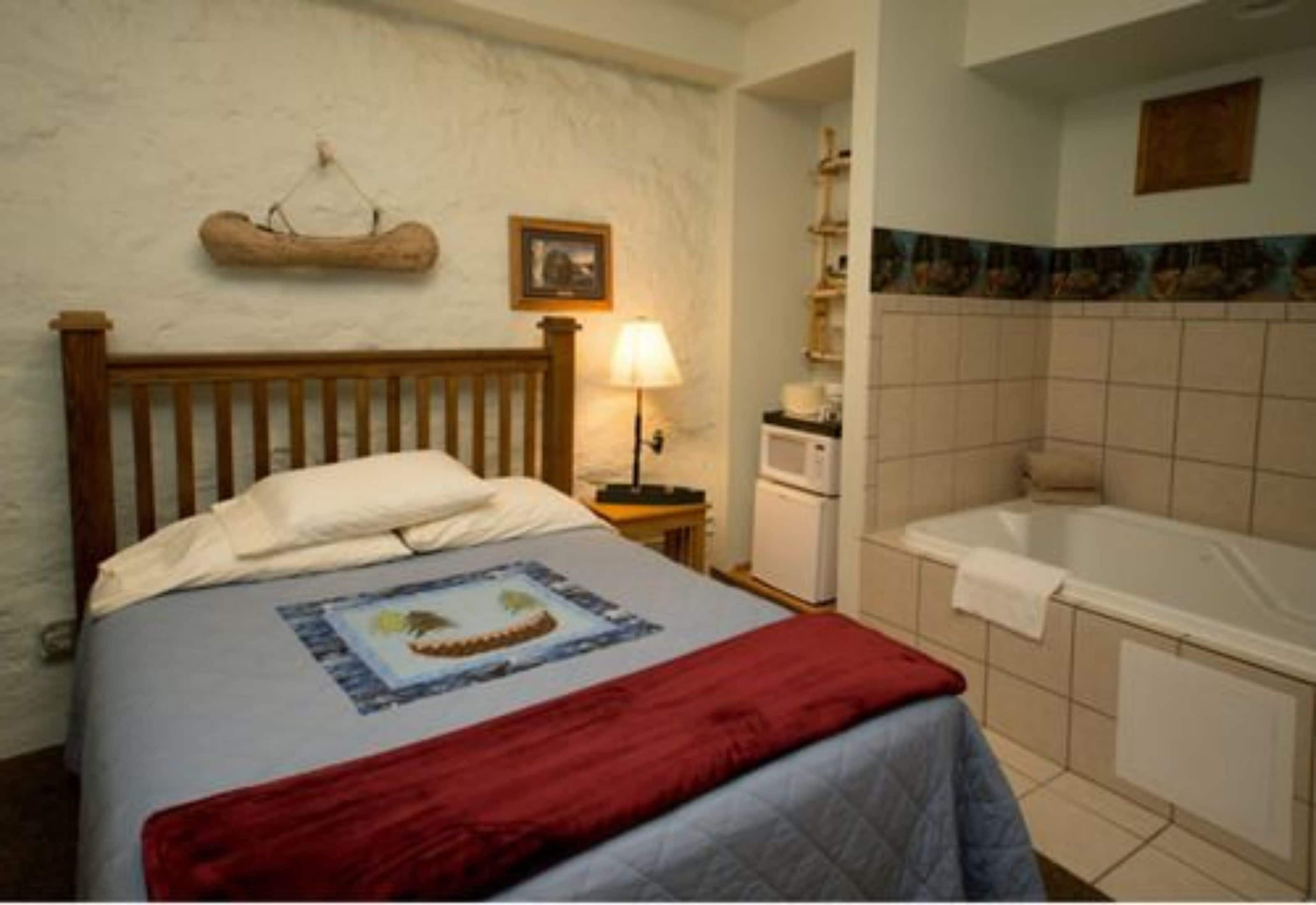 Una camera da letto con un letto di legno, un comodino con una lampada, un bagno con una vasca e un muro rivestito di piastrelle.