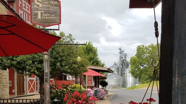 An outdoor seating area with wicker chairs and tables, surrounded by vibrant flowers and a red umbrella. - Stone Mill Hotel & Suites (Lanesboro)