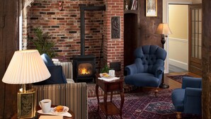 A cozy living room with a brick fireplace, a blue armchair, a striped sofa, and a wooden coffee table. - 1802 House Bed and Breakfast (Kennebunkport)