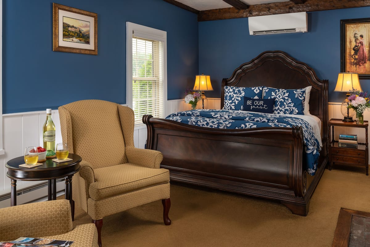A bedroom with a large bed, two bedside tables with lamps, a chair, and a small table with a bottle and glasses.