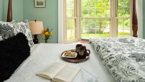A neatly made bed with a tray of cookies and two mugs, a book, and a lamp on a bedside table. - 1802 House Bed and Breakfast (Kennebunkport)