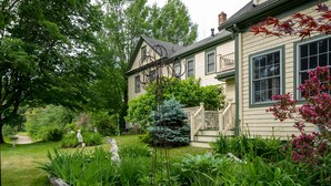 A house with a well-maintained garden, a wooden deck, and a statue in the yard. - 1802 House Bed and Breakfast (Kennebunkport)