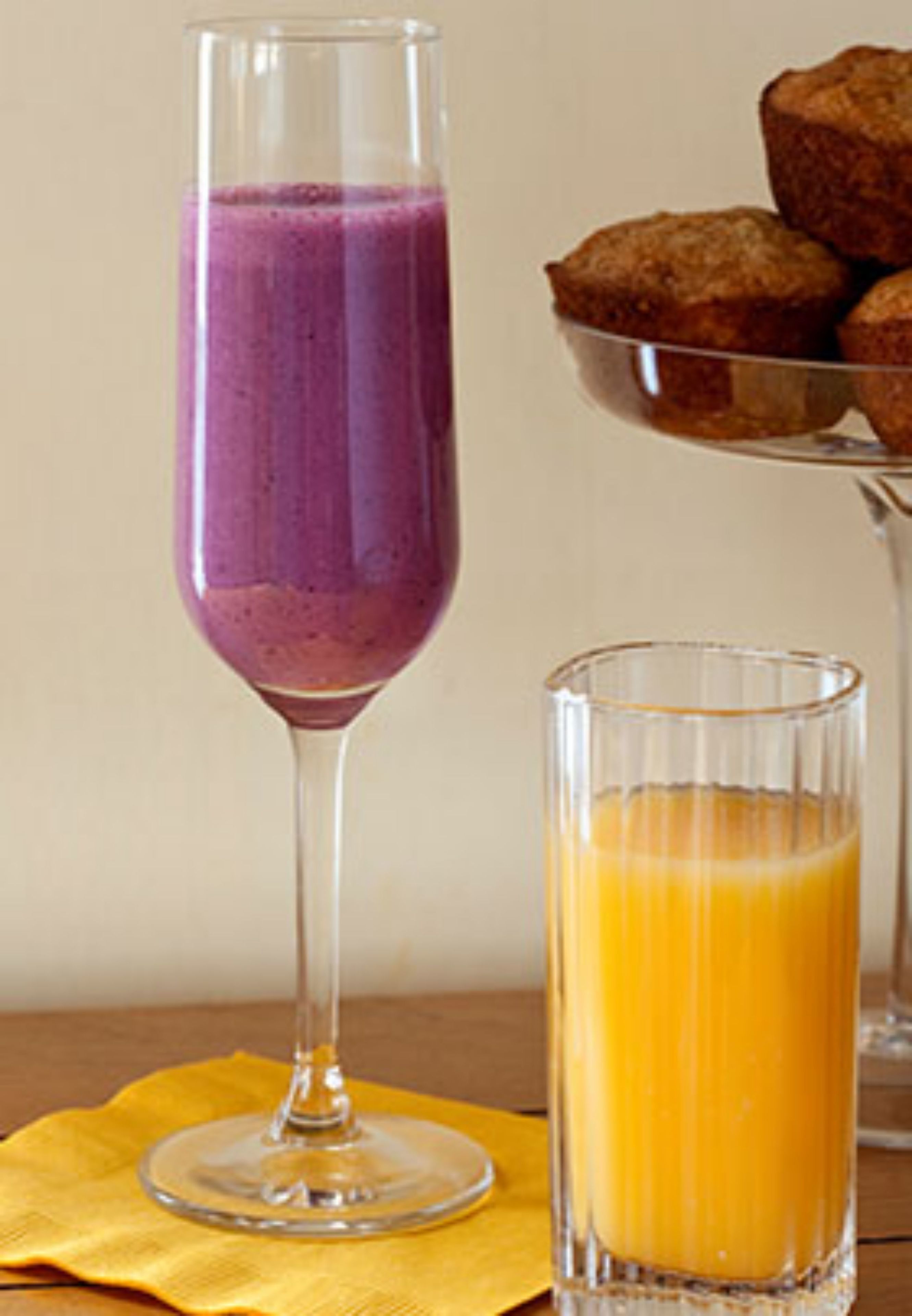Un vaso de batido morado y un vaso de jugo de naranja sobre una servilleta amarilla.