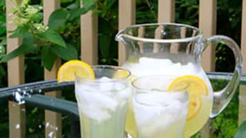 A glass pitcher and two glasses of lemonade with lemon slices on a table outdoors.