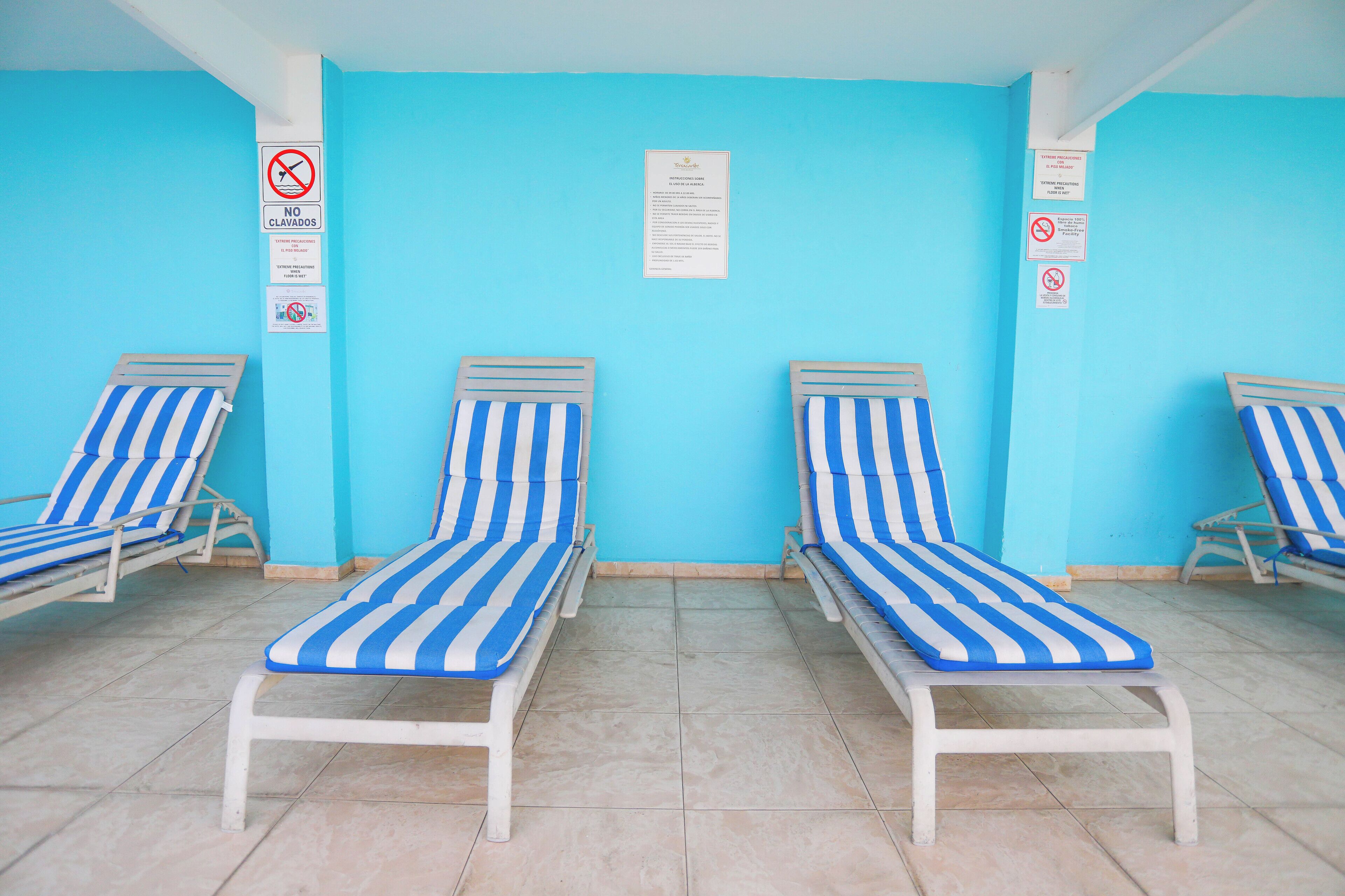 A poolside area with blue and white striped lounge chairs, a tiled floor, and several signs on the walls.