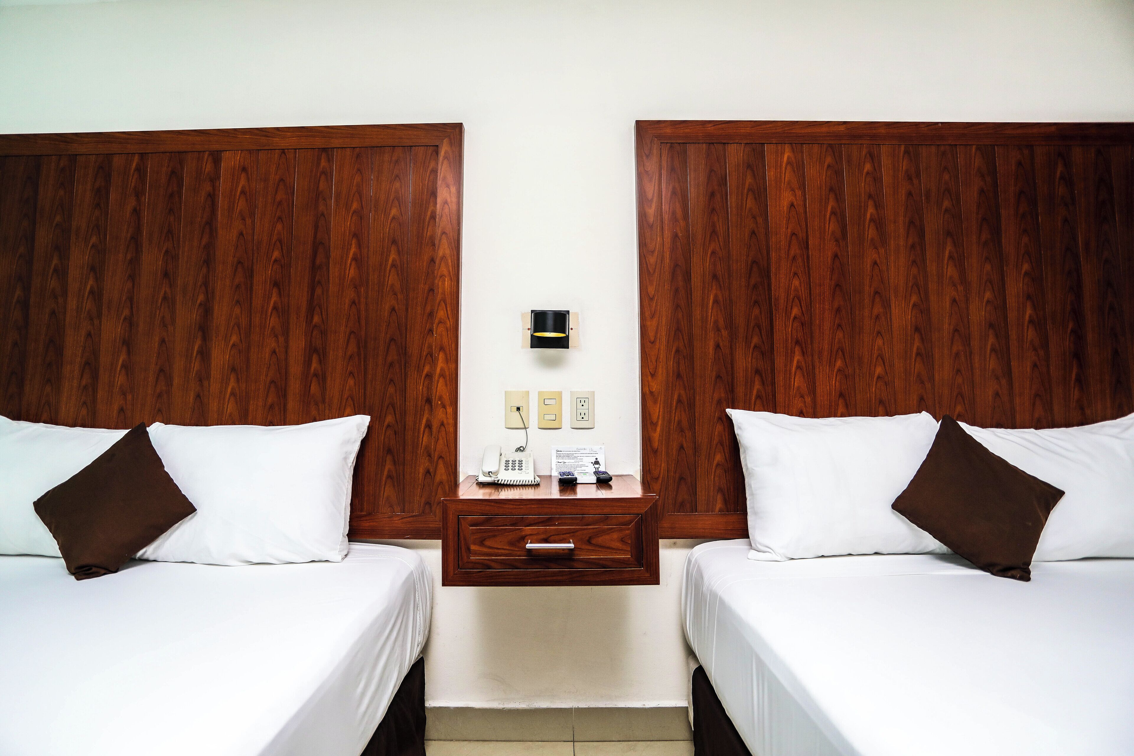 A hotel room with two beds, a wooden headboard, a nightstand with a telephone, and a wall socket.