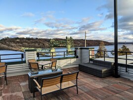An outdoor terrace with a view of a bridge and hills, furnished with wooden chairs and a table.