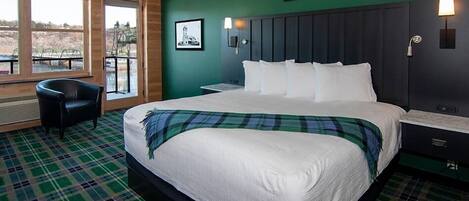A hotel room with a large bed, a chair, a nightstand, and a view of the outdoors through a window.