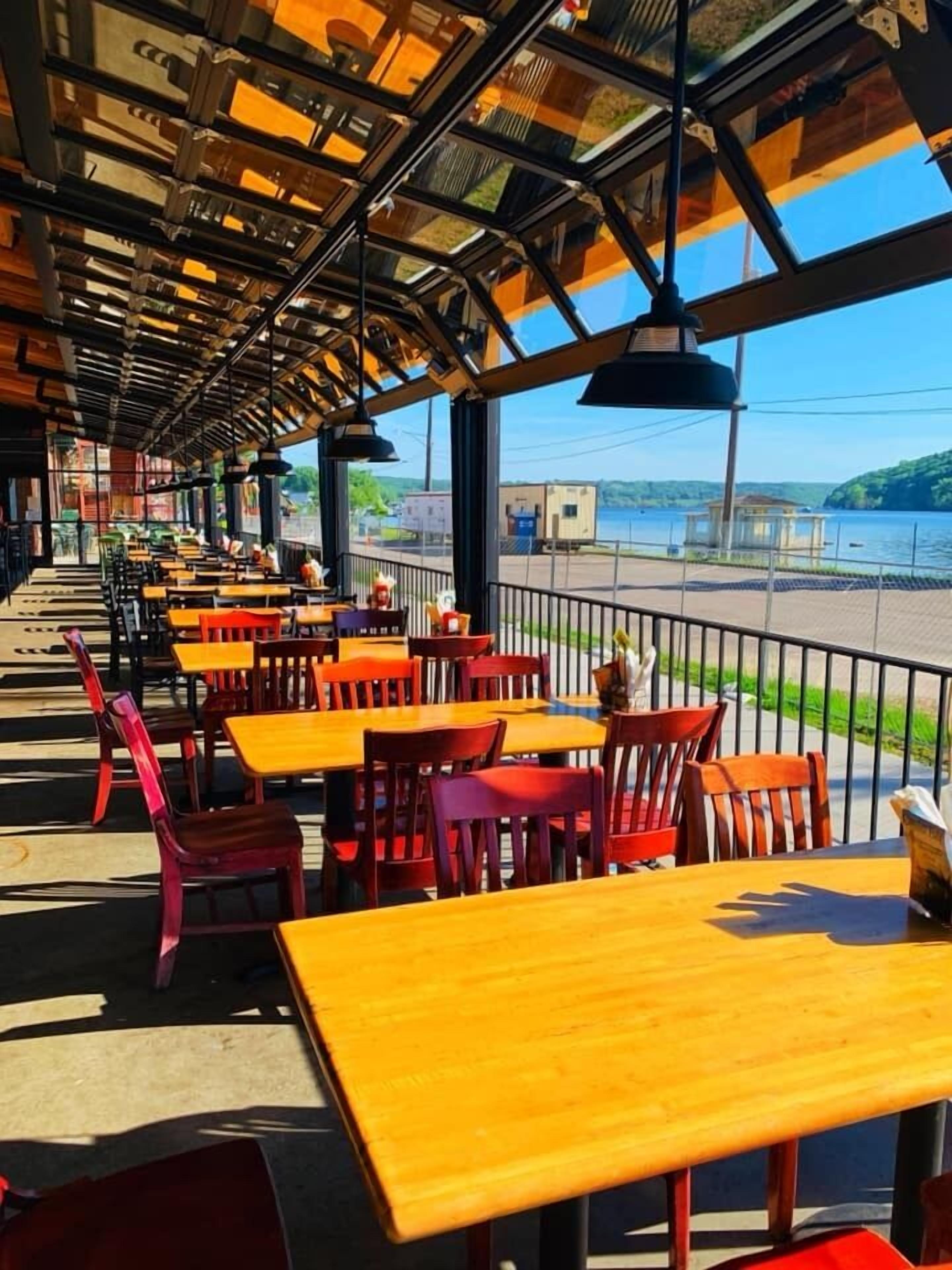 A covered outdoor seating area with tables and chairs, overlooking a body of water.