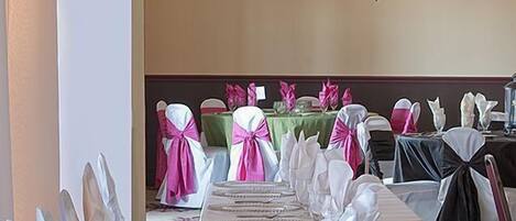 A banquet hall with white tablecloths, chairs with white and pink sashes, and a chandelier.