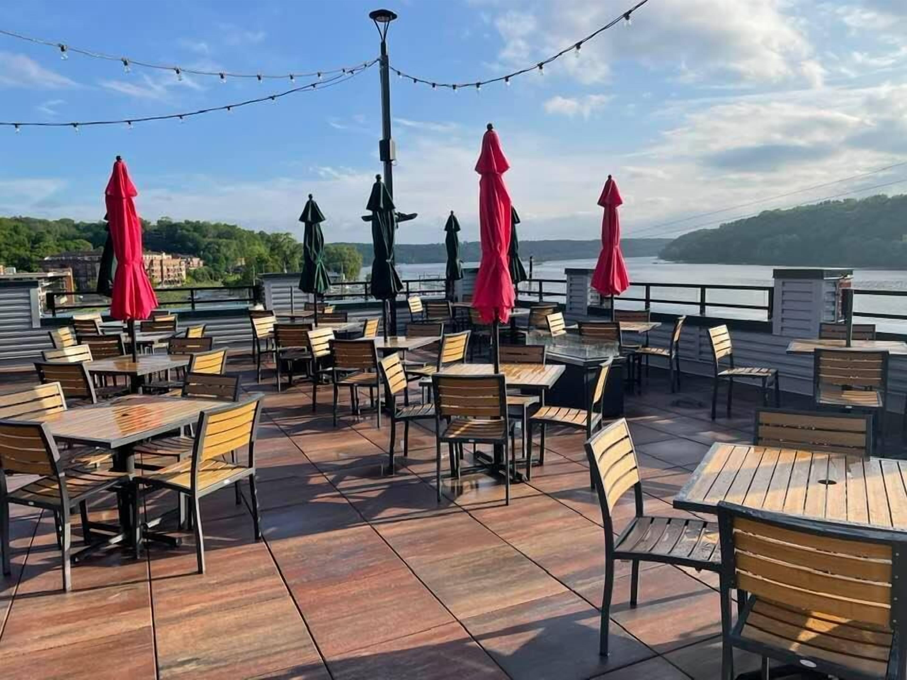 Een terras buiten met houten tafels en stoelen, rode parasols en lichtjes.
