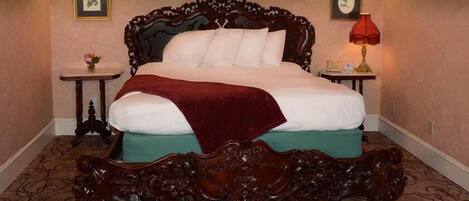 Una cama grande y ornamentada con estructura de madera oscura y colchón blanco, flanqueada por dos mesitas de noche con lámparas.