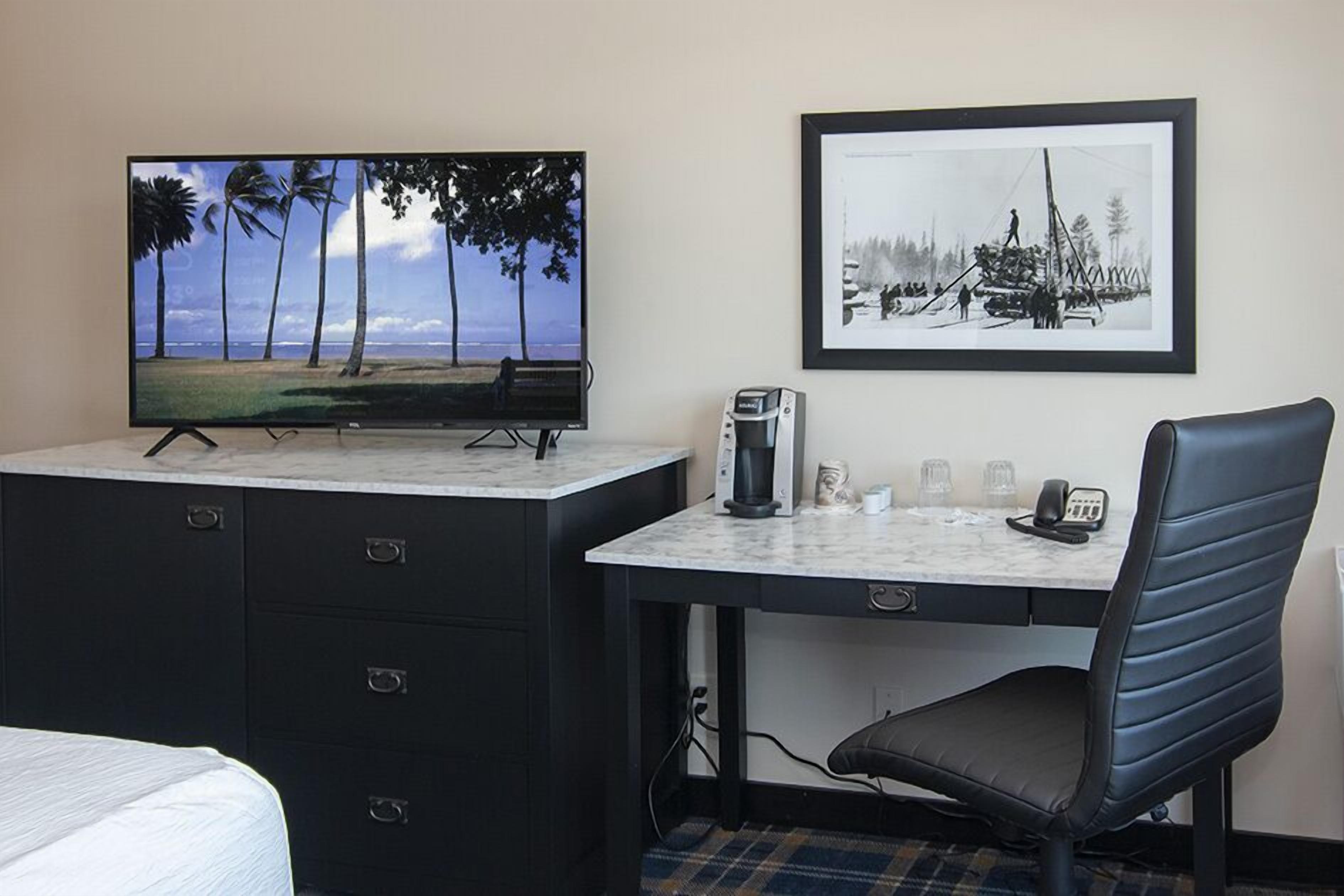 Une chambre d’hôtel avec un lit, un bureau équipé d’un ordinateur, une télévision et un tableau encadré au mur.