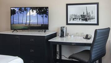 Une chambre d’hôtel avec un lit, un bureau équipé d’un ordinateur, une télévision et un tableau encadré au mur.