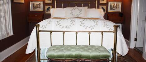 Un dormitorio con una cama con dosel, un banco tapizado de color verde y una colcha estampada.