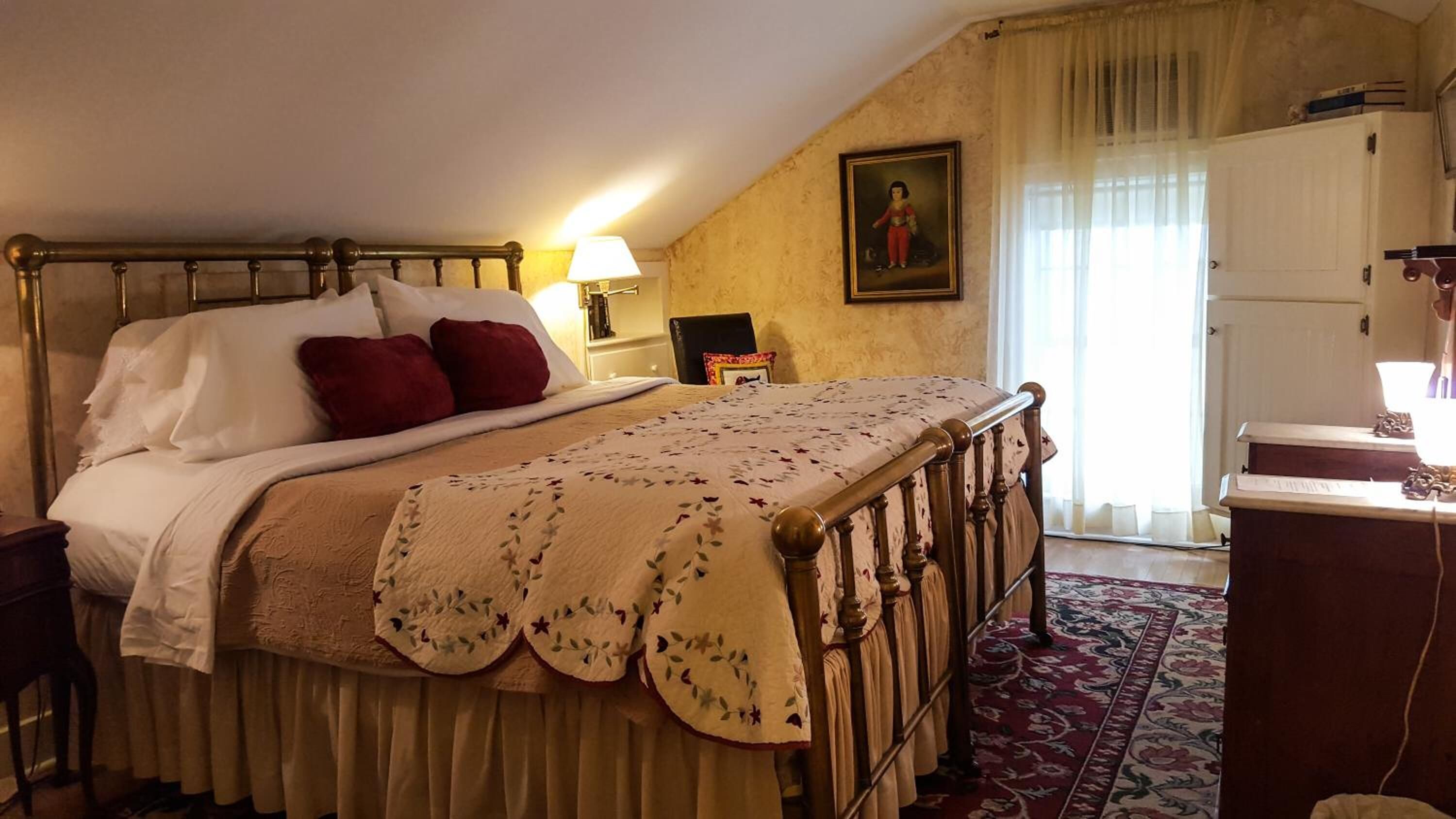 A bedroom with a bed, a desk, a chair, a lamp, and a painting on the wall.