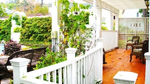A covered porch with white railings, wicker furniture, and a view of a lush garden. - The White House Inn (Cooperstown)