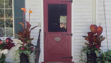 A white building with a red door labeled "Entrance." There are two potted plants on either side of the door.