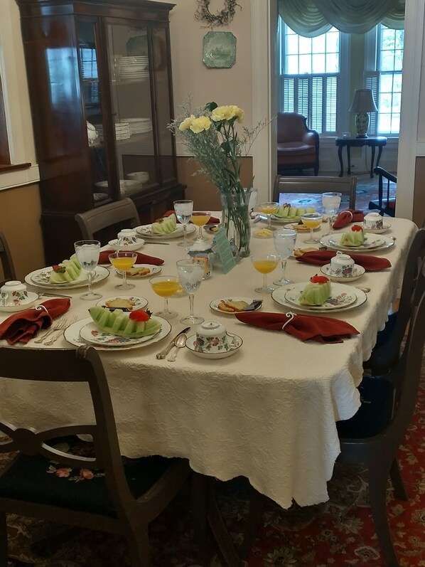 A dining table set with plates, cutlery, and various dishes including fruit and beverages. - The White House Inn (Cooperstown)