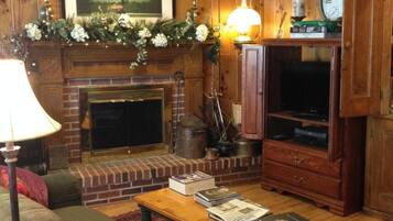 A cozy living room with a fireplace, a ceiling fan, a clock, and a bookshelf.