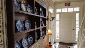 A hallway with a display of blue and white plates on shelves, a lamp, and a door with an exit sign. - The White House Inn (Cooperstown)