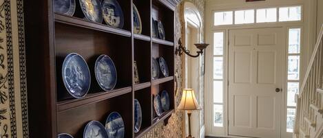 A hallway with a display of blue and white plates on shelves, a lamp, and a door with an exit sign.