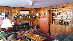 A cozy living room with a fireplace, wooden walls, a coffee station, and a clock. - The White House Inn (Cooperstown)
