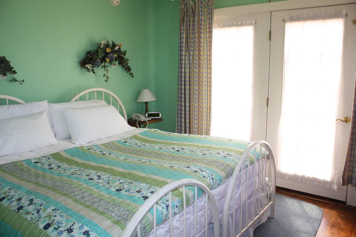 A bedroom with a bed, a nightstand, a lamp, and a window with curtains.