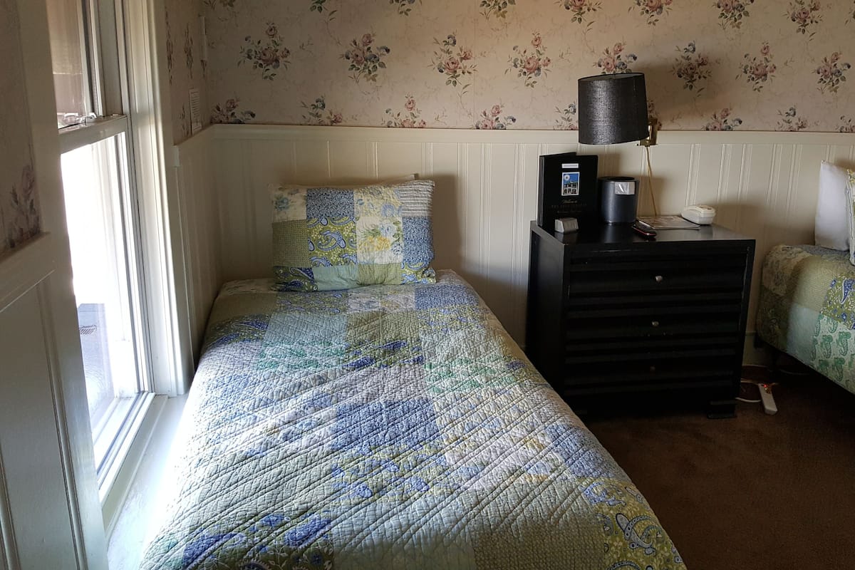 Une chambre avec deux lits simples, une commode, une lampe et un thermostat.
