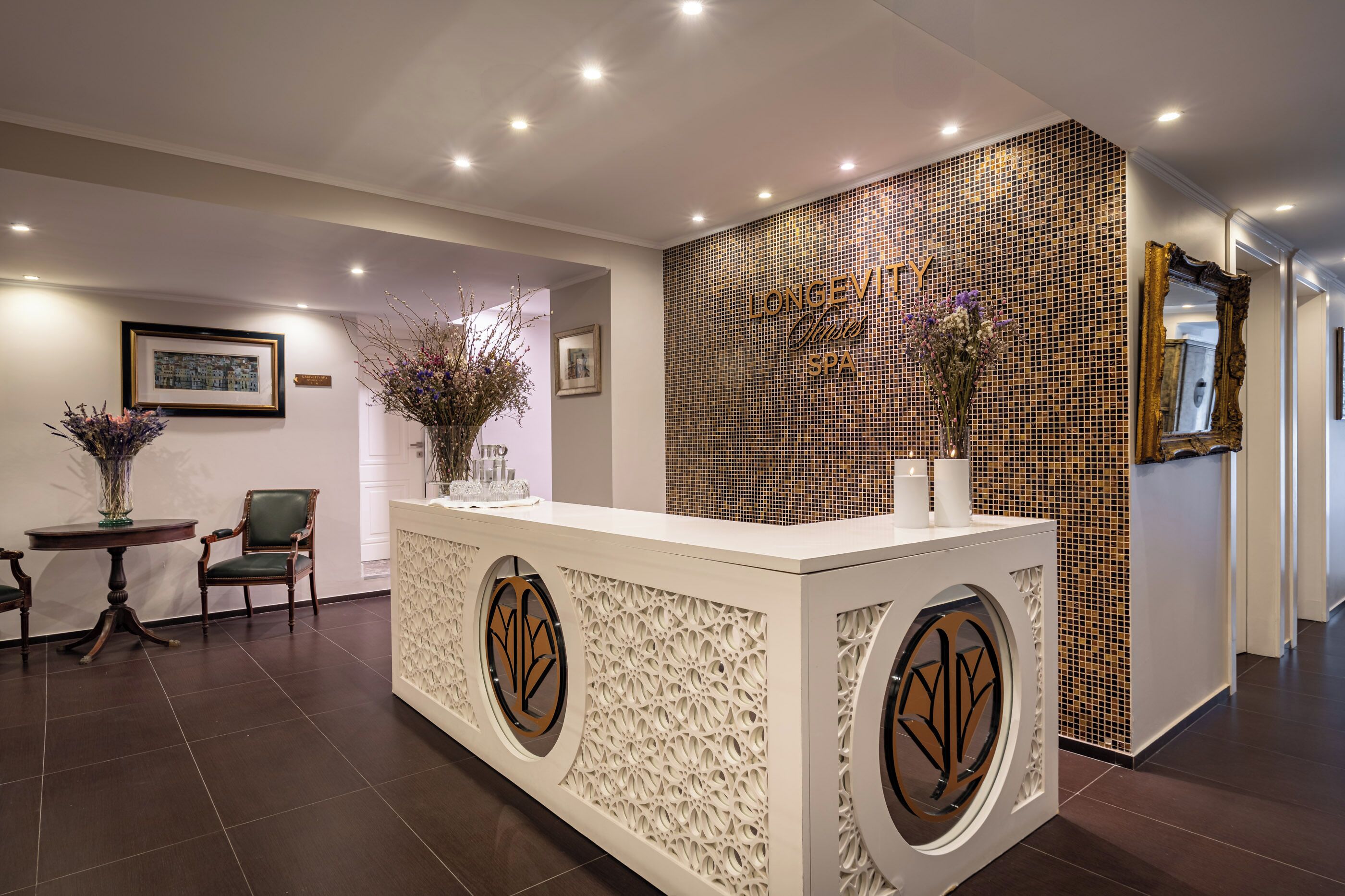 A reception area with a white reception desk, framed artwork on the wall, and a decorative vase with flowers.
