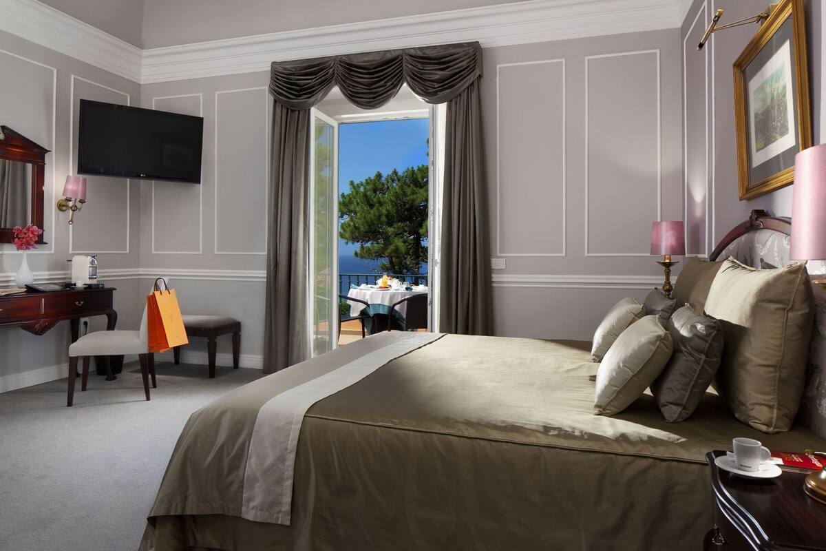 A hotel room with a bed, a desk, a chair, a TV, and a view of the outdoors.