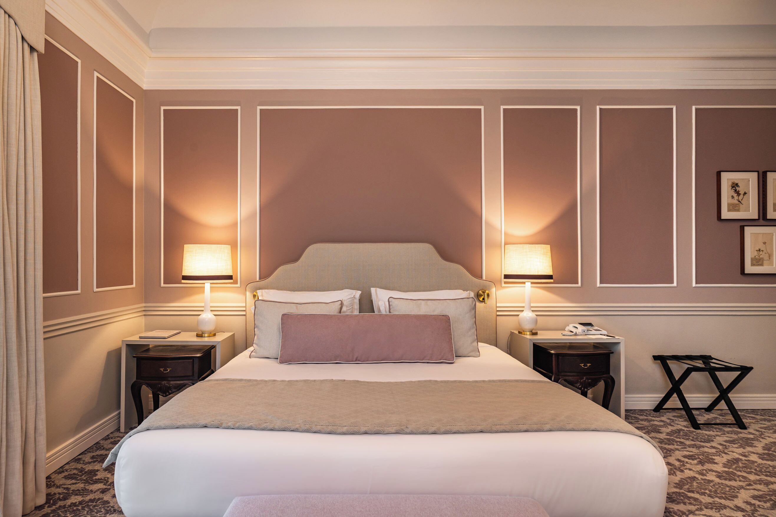 A neatly arranged hotel room with a large bed, two bedside tables with lamps, a small side table, and a patterned carpet.
