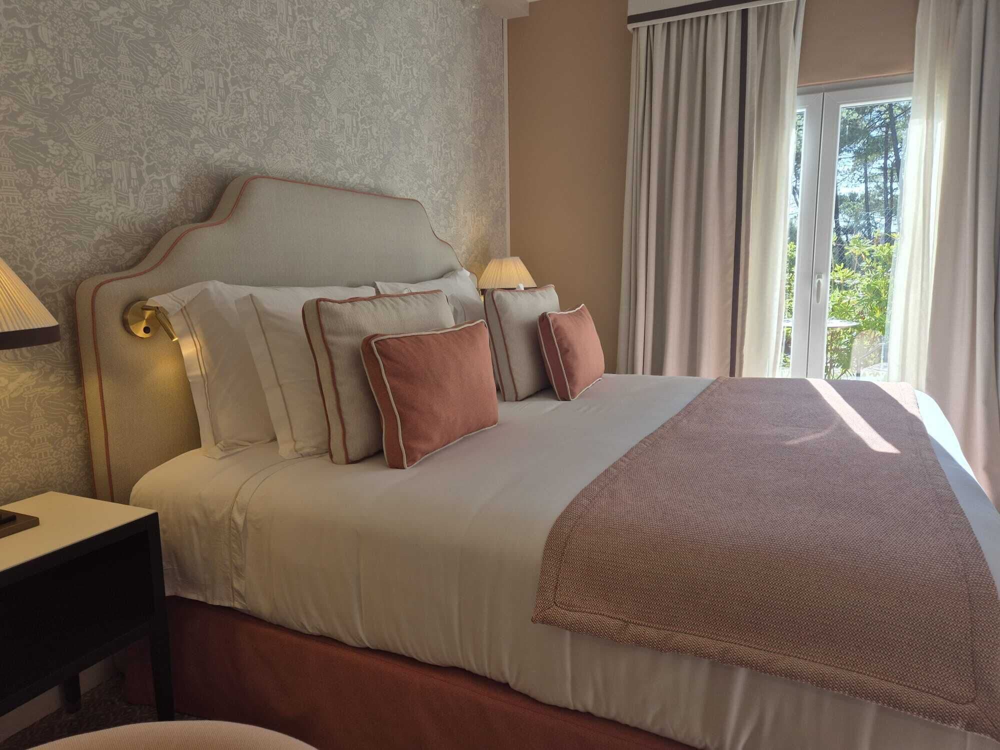 A hotel room with a large bed, a nightstand, a lamp, and a window with curtains.