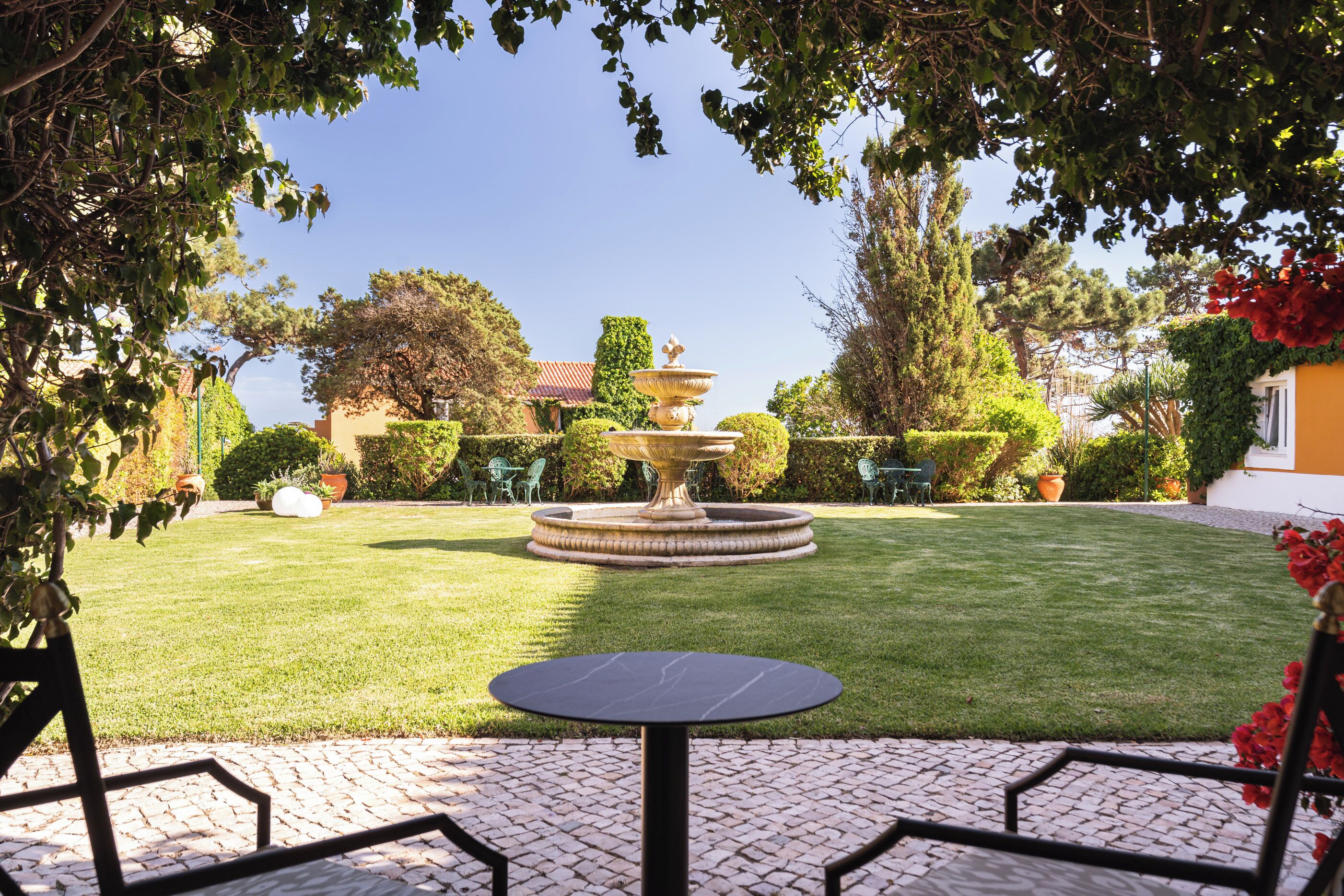 Ein Garten mit Brunnen, gepflasterter Terrasse und Rasenfläche.