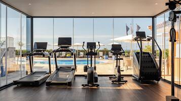 A modern gym with treadmills, elliptical machines, and a rowing machine, overlooking a pool and outdoor area.
