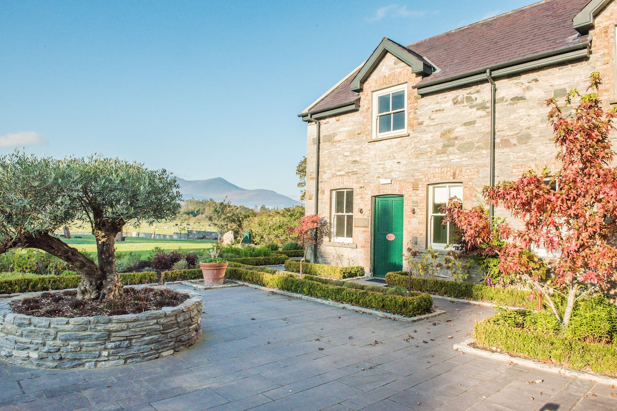 A stone building with a green door, a well-maintained garden, and a view of distant mountains.