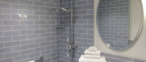 A bathroom with blue-tiled walls, a white sink, a round mirror, and a towel rack with folded towels.