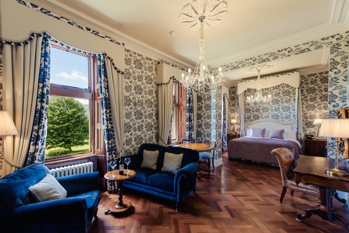 A room with a large bed, a blue sofa, a wooden coffee table, and a chandelier.