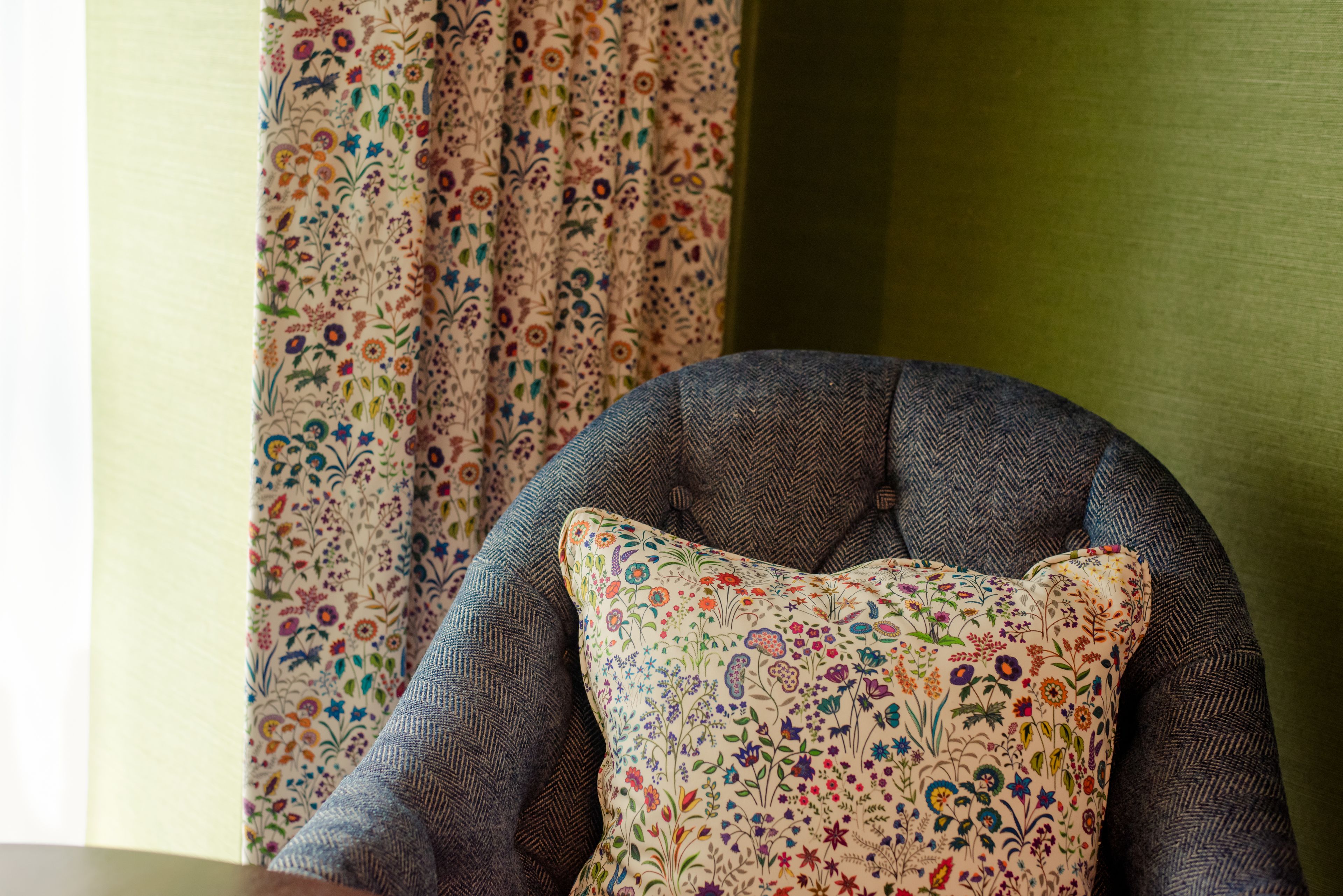 Ein Stuhl mit einem floralen Kissen und einem gemusterten Vorhang im Hintergrund.