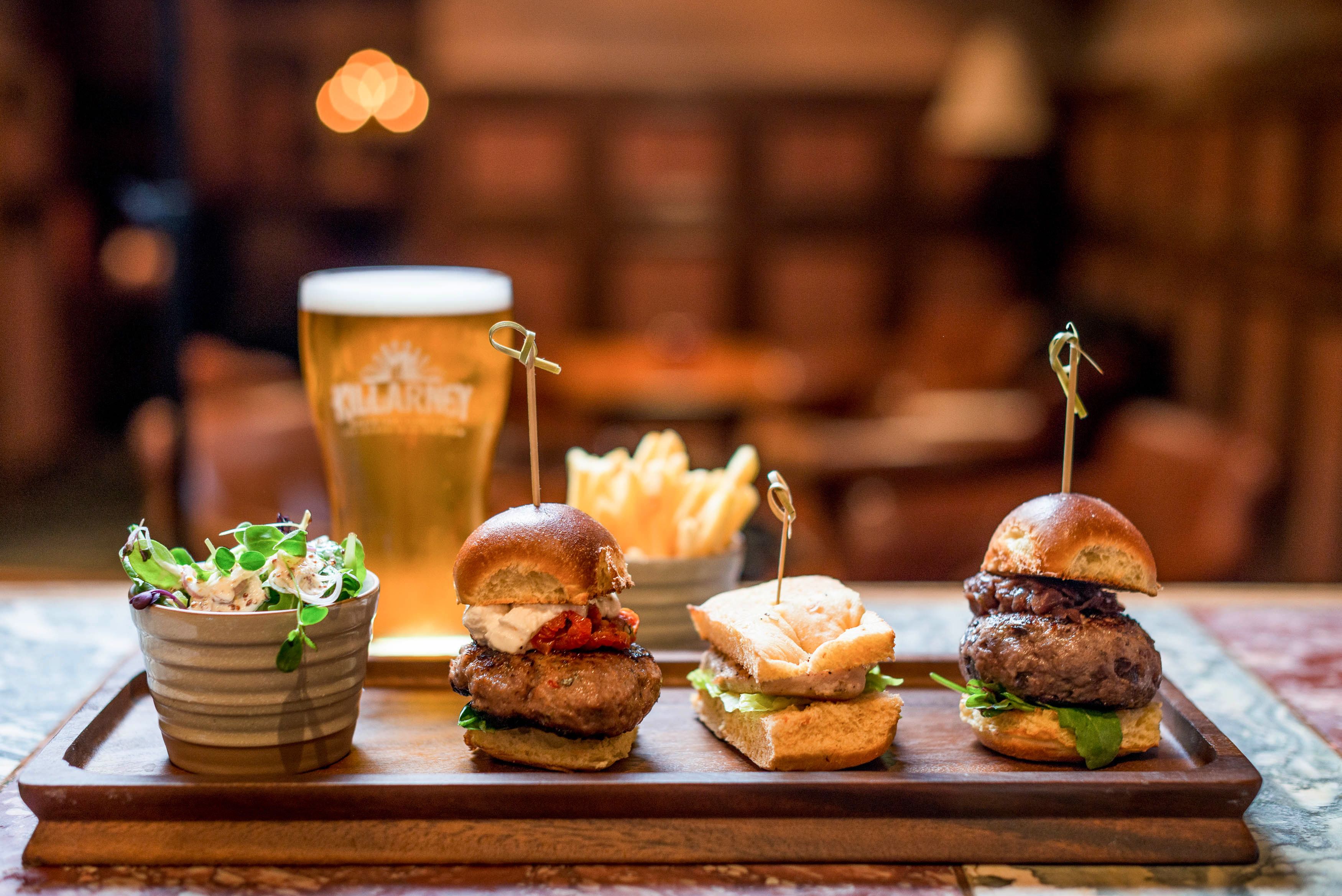 A tray with two burgers, a bowl of salad, and a glass of beer.