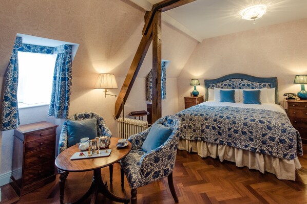 A bedroom with a large bed, a wooden chair, a table with a tray, and a window with curtains.