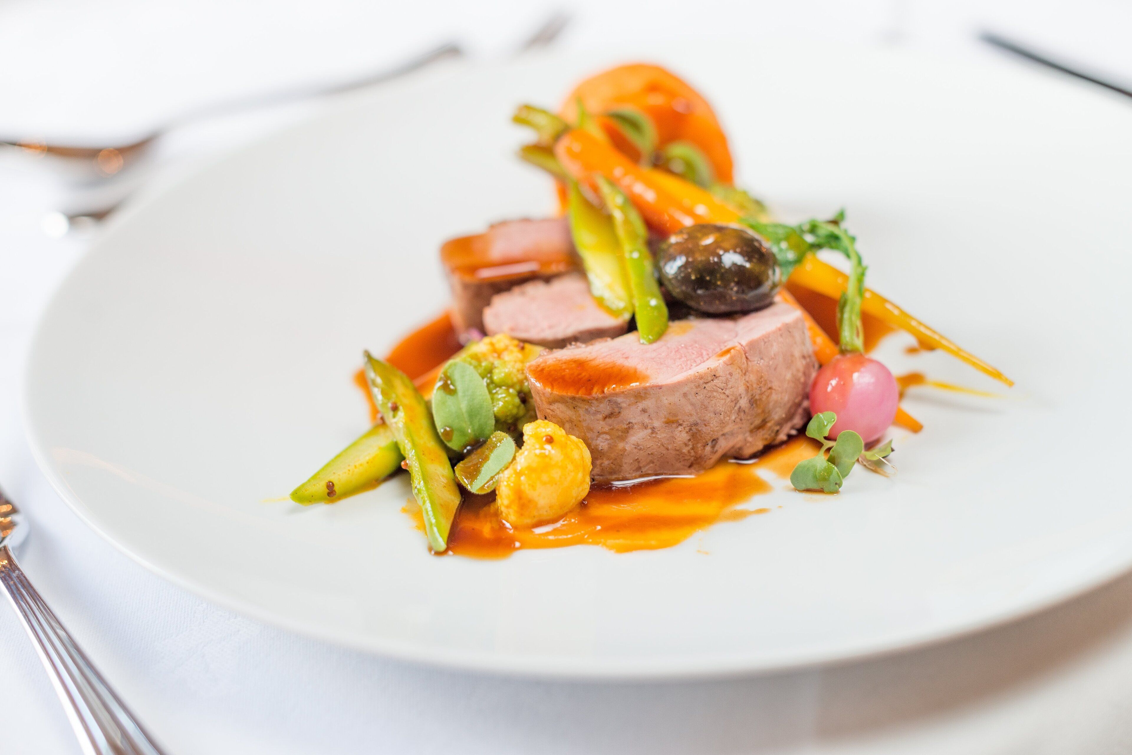 A white plate with a meat dish, vegetables, and sauce.