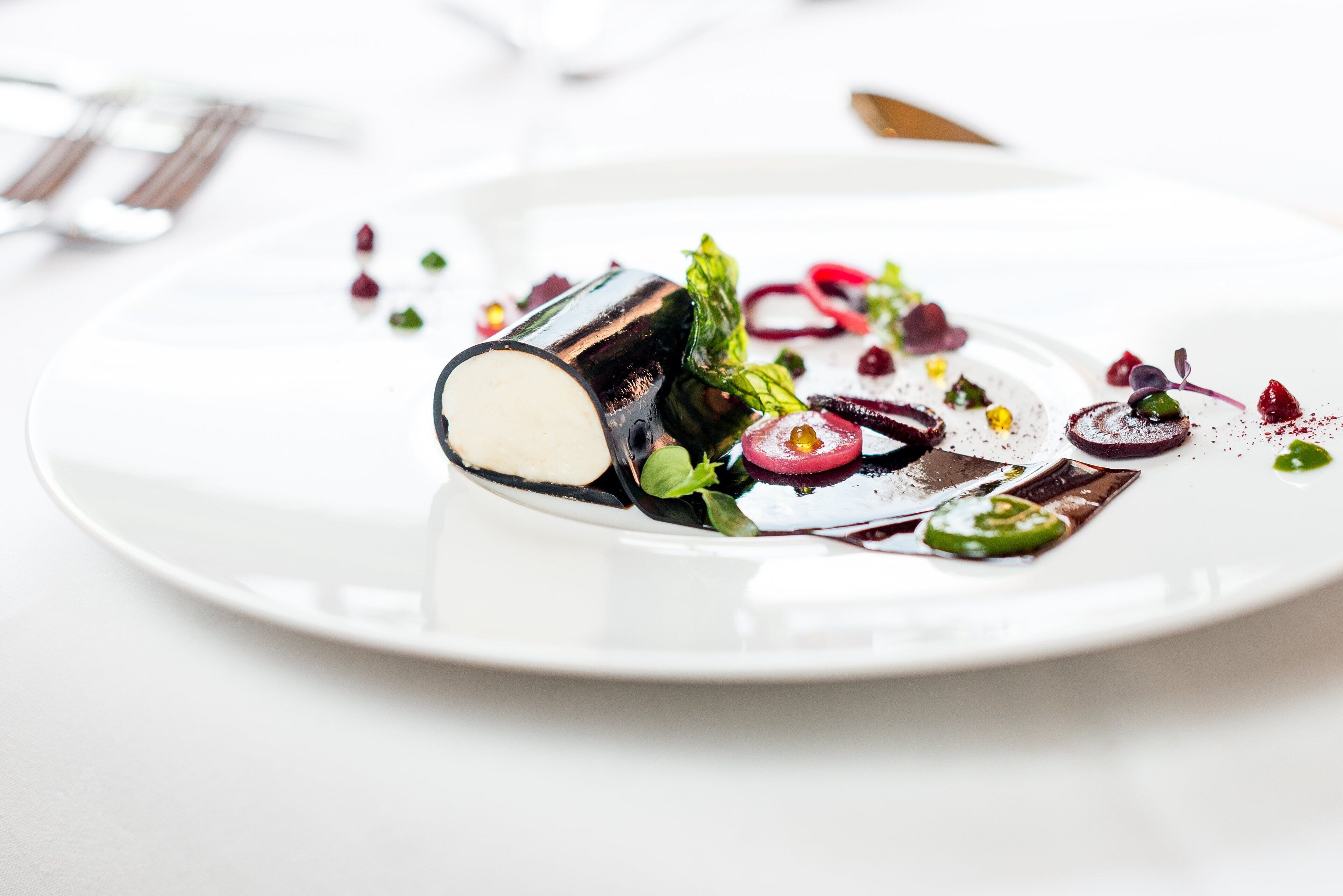 A white plate with a dessert featuring a chocolate element, green leaves, and red berries.
