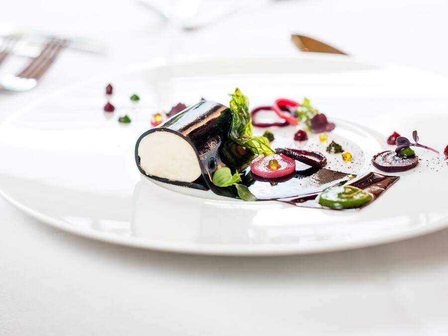 A white plate with a dessert featuring a chocolate element, green leaves, and red berries.