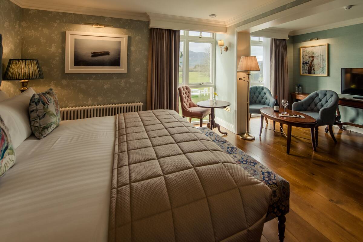 A hotel room with a large bed, a sitting area with a table and chairs, a radiator, and a window with curtains.