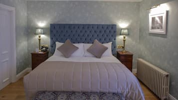 A bedroom with a tufted headboard, two bedside tables with lamps, a patterned bedspread, and a radiator.
