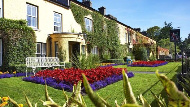 Una hilera de casas tradicionales con un jardín cuidado, con coloridos macizos de flores y un banco de metal blanco.