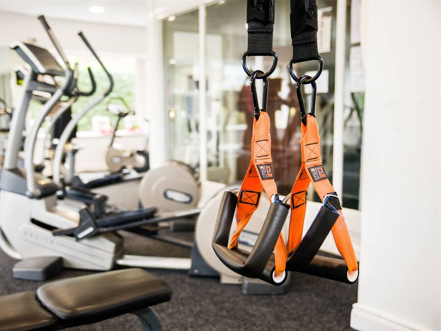 A gym with exercise equipment including treadmills, a bench, and TRX suspension straps.